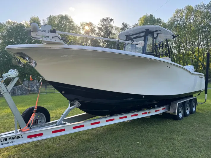 Yacht Photos Pics 2024 Tidewater 292 CC Adventure boat on trailer, parked on grass with trees in background.