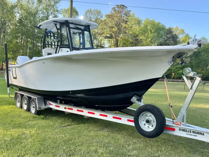  Yacht Photos Pics 2024 Tidewater 292 CC Adventure boat on trailer, parked on grass with trees in background.