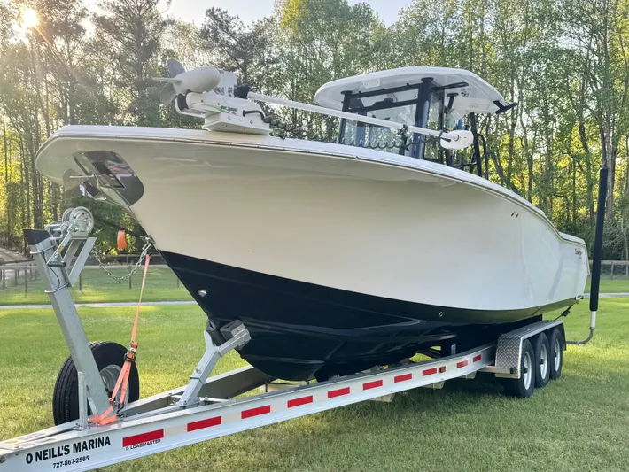  Yacht Photos Pics 2024 Tidewater 292 CC Adventure boat on trailer, parked on grass with trees in background.