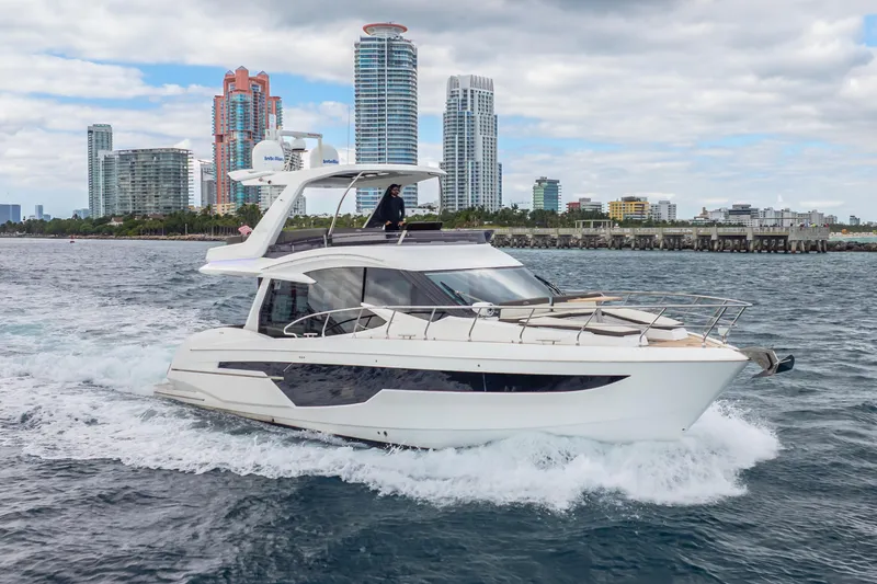 Infinity Yacht Photos Pics 2020 Galeon 500 Fly yacht cruising near city skyline, under cloudy sky.