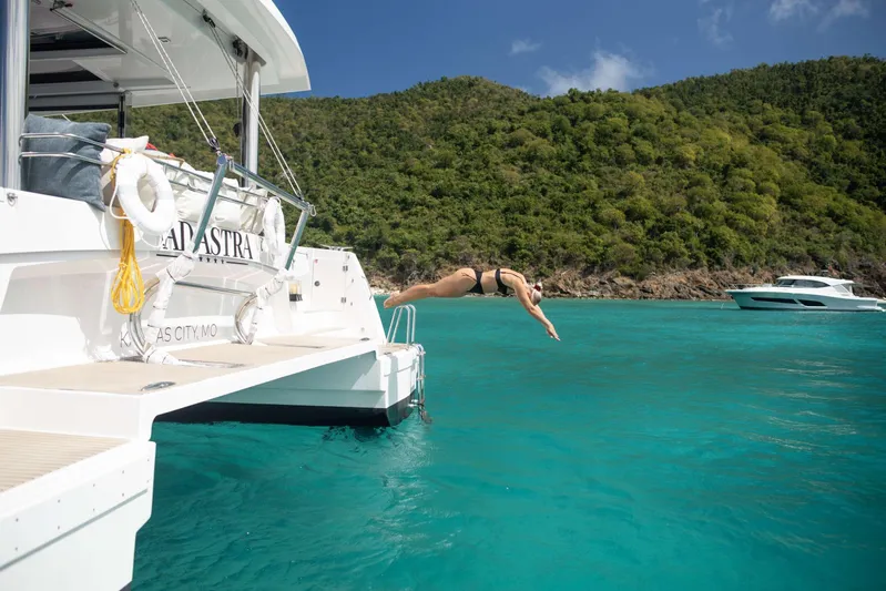 Ad Astra Yacht Photos Pics Person diving off Bali 5.4 catamaran into turquoise water, lush hills in background.