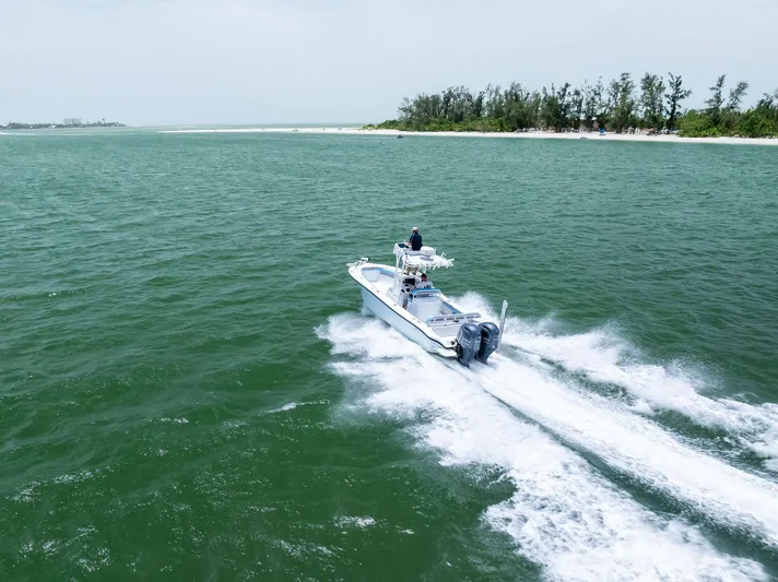  Yacht Photos Pics 2016 Yellowfin 26 Hybrid boat cruising on open water near a forested shoreline.