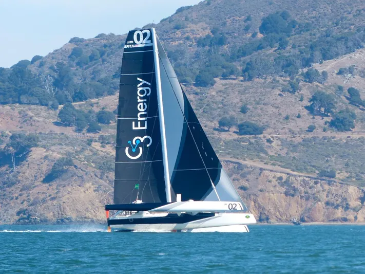  Yacht Photos Pics Sailing yacht CDK Technologies MOD70, 2011, gliding on water with scenic mountain backdrop.