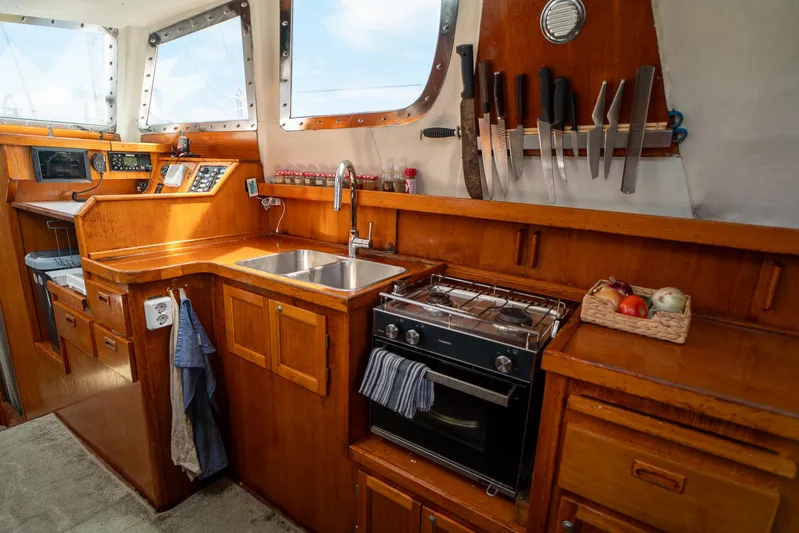 See The World Yacht Photos Pics Compact boat kitchen with wooden cabinetry, dual sink, stove, and knife rack, Custom 49 model, 1998.