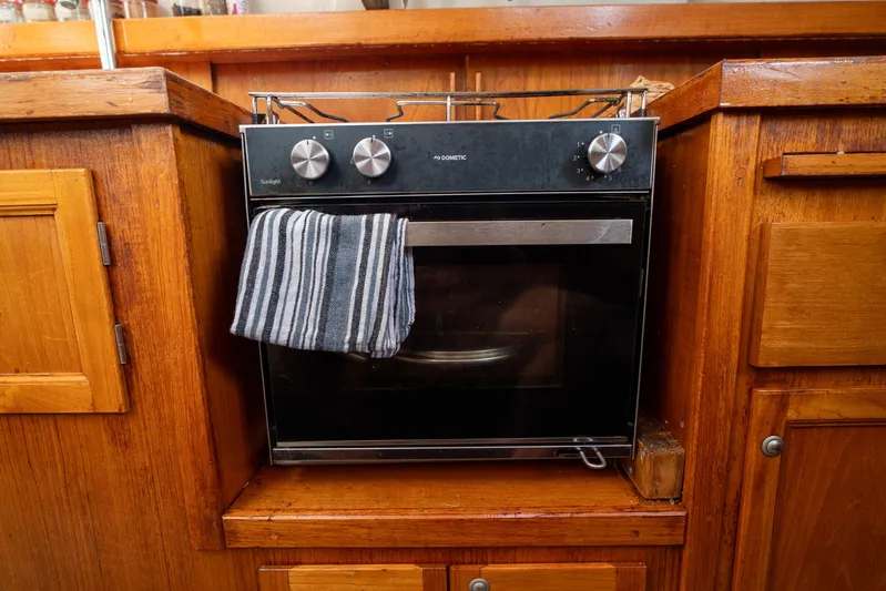 See The World Yacht Photos Pics Built-in black oven with striped towel, surrounded by wooden cabinetry.