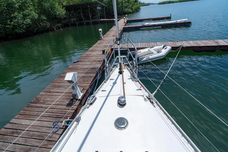 See The World Yacht Photos Pics Sailboat docked at wooden pier with inflatable dinghy, surrounded by lush greenery.