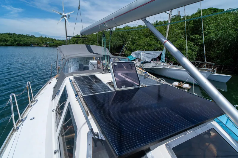 See The World Yacht Photos Pics Sailboat with solar panels and wind turbine, Custom 49 model, 1998, docked by lush greenery.