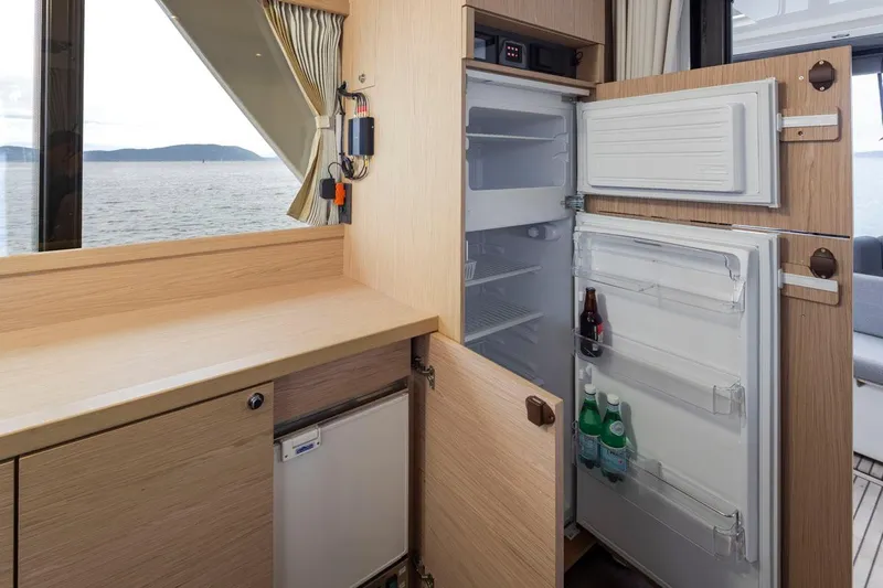 4 My Valentine Yacht Photos Pics 2022 Beneteau Swift Trawler 41 interior with open fridge, wooden cabinetry, and ocean view.