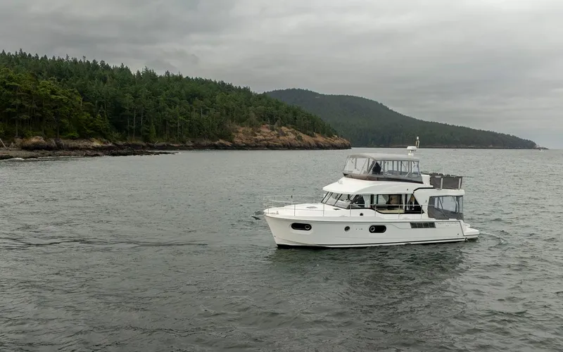 4 My Valentine Yacht Photos Pics 2022 Beneteau Swift Trawler 41 cruising near forested coastline under cloudy skies.