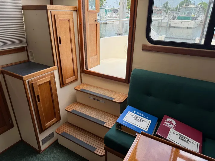Emerald Isle Yacht Photos Pics Interior of a 1998 Nordic Tug Trawler with wooden cabinetry and manuals on a green seat.