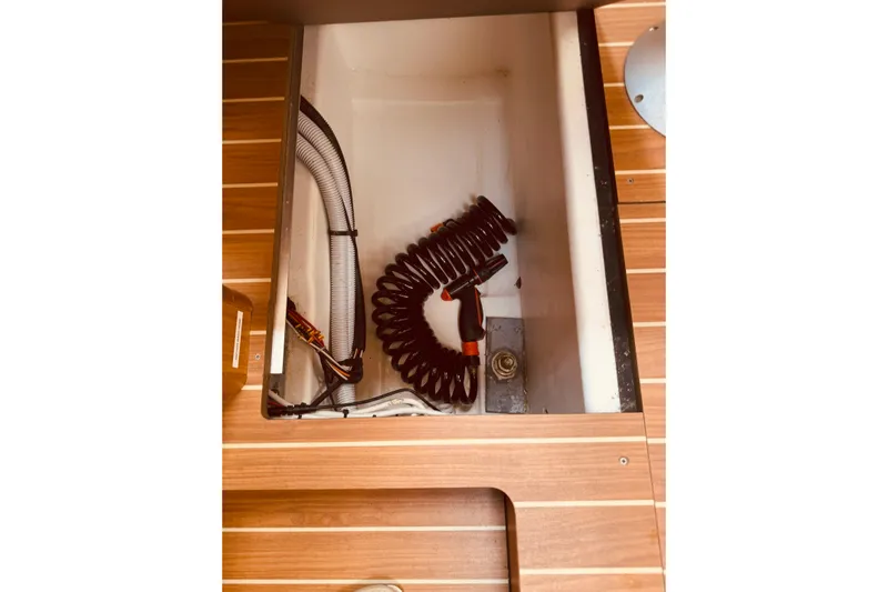 Bluefin Yacht Photos Pics Storage compartment on 2008 Jeanneau Sun Odyssey 45 DS sailboat with coiled hose and wooden flooring.