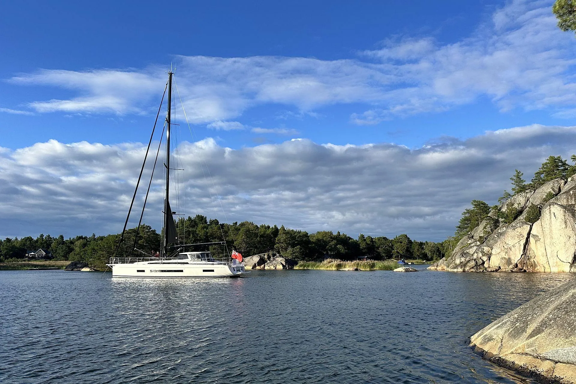 2023 Amel 60 sailboat in a serene bay with rocks and trees.