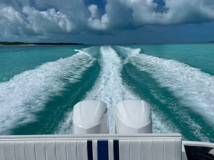  Yacht Photos Pics Intrepid 32 boat cruising on turquoise waters, leaving a wake trail, under a cloudy sky.