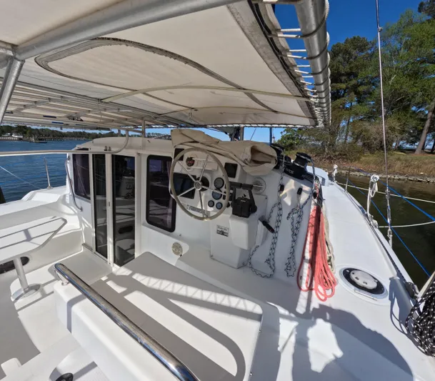 Quelle Belle Vie Yacht Photos Pics 2008 Fountaine Pajot Mahe 36 catamaran cockpit with steering wheel and canopy, docked by trees.