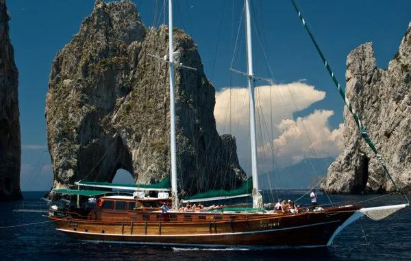  Yacht Photos Pics Classic 2006 Caicco ERDAL SOGUTCU sailing near rocky cliffs under a clear blue sky.