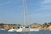 Custom 22m Catamaran 2023 sailing near rocky coastline under clear blue sky.