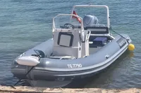Inflatable boat docked by the shore, featuring a steering console and outboard motor.