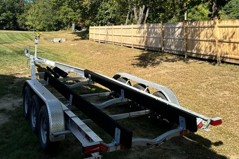  Yacht Photos Pics Trailer for 2023 Sailfish 312 CC boat, parked on grass near wooden fence.