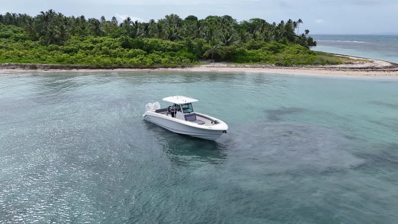  Yacht Photos Pics 2025 Boston Whaler 330 Outrage boat near tropical island with lush greenery and clear waters.