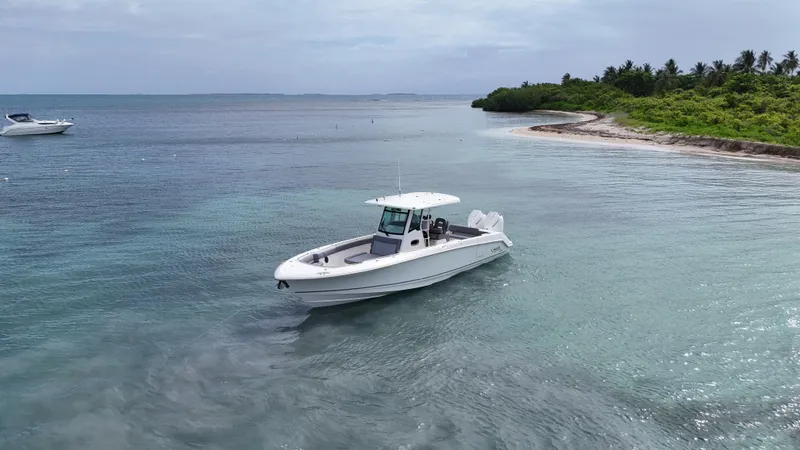  Yacht Photos Pics 2025 Boston Whaler 330 Outrage boat near tropical shoreline, calm waters, and lush greenery.