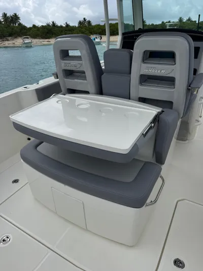  Yacht Photos Pics 2025 Boston Whaler 330 Outrage boat seating with foldable table, near scenic shoreline.
