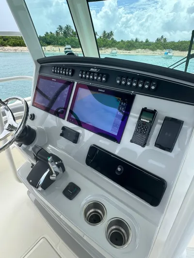  Yacht Photos Pics 2025 Boston Whaler 330 Outrage helm with dual screens and control panel, docked by a scenic shoreline.