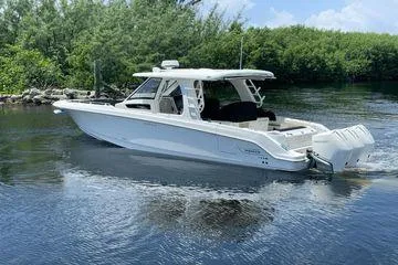  Yacht Photos Pics 2022 Boston Whaler 350 Realm boat on calm water, surrounded by lush greenery.