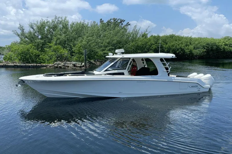  Yacht Photos Pics 2022 Boston Whaler 350 Realm boat on calm water, surrounded by lush greenery.