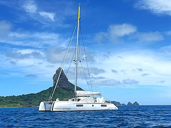 Traverse Yacht Photos Pics Sailing catamaran Outremer 51, 2021 model, on blue ocean with scenic rocky island backdrop.