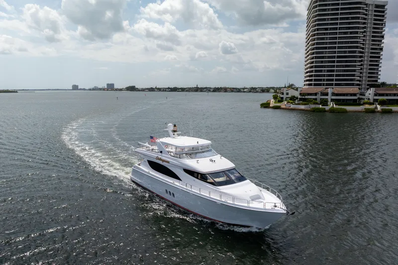Outrageous Yacht Photos Pics 2005 Hatteras 80 Motor Yacht cruising near waterfront buildings under cloudy sky.