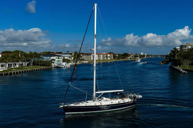 Windigo Yacht Photos Pics Sailing yacht Beneteau 50 (2003) cruising on a scenic waterway under a clear blue sky.