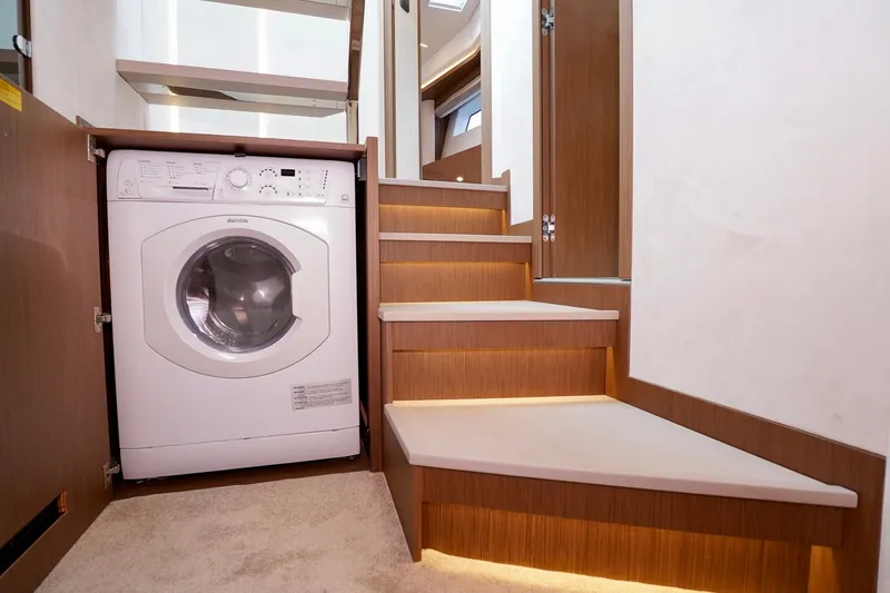 Yacht Photos Pics Compact laundry area with washing machine under wooden stairs, Prestige F5.7, 2025 model.