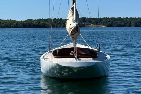 2010 Rustler 24 sailboat on calm water, forested shoreline in background.