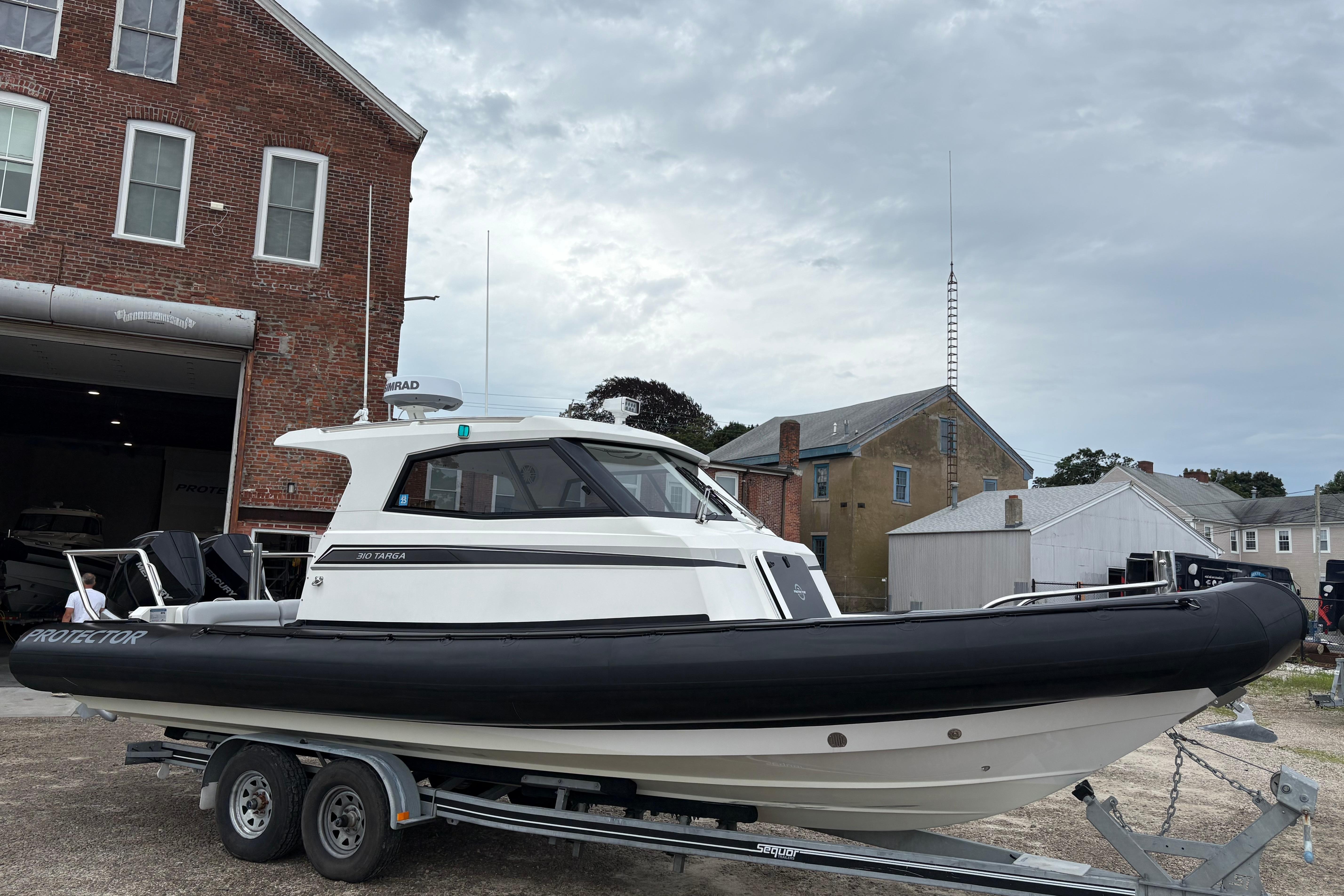 2020 Protector 310 Targa boat on trailer, parked near brick building.