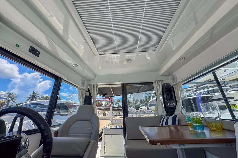  Yacht Photos Pics Interior of 2018 Jeanneau NC 895 boat with seating, table, and glassware under a sunny sky.