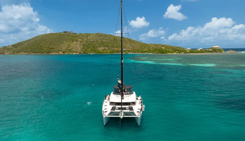 Respite At Sea Yacht Photos Pics 2018 Lagoon 560 catamaran sailing in turquoise waters near a lush island.