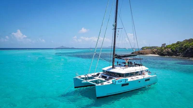 Respite At Sea Yacht Photos Pics 2018 Lagoon 560 catamaran sailing in clear turquoise waters near a tropical island.