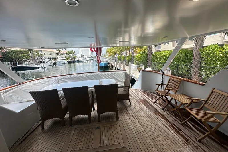 Adventurer Yacht Photos Pics Luxury yacht deck with wicker chairs, wooden flooring, and marina view, Burger 94 model, 1985.