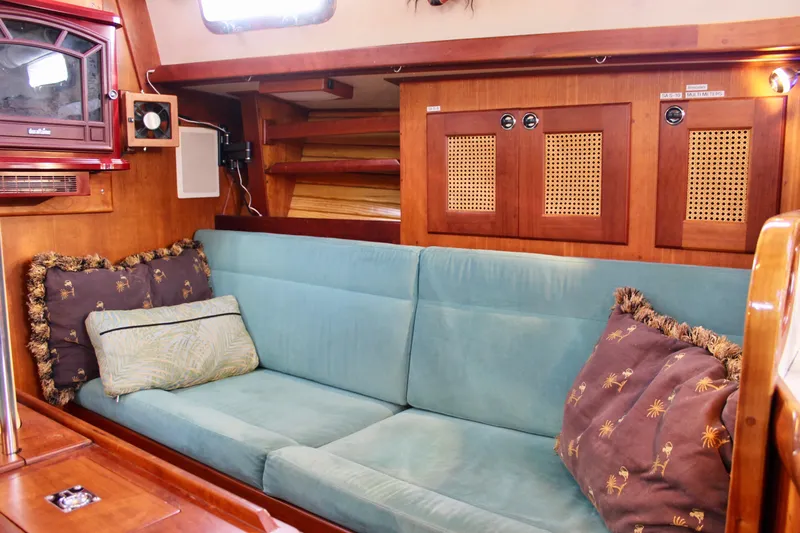 Mangata Yacht Photos Pics 1997 Valiant 39 yacht interior with teal sofa, decorative pillows, and wooden cabinetry.