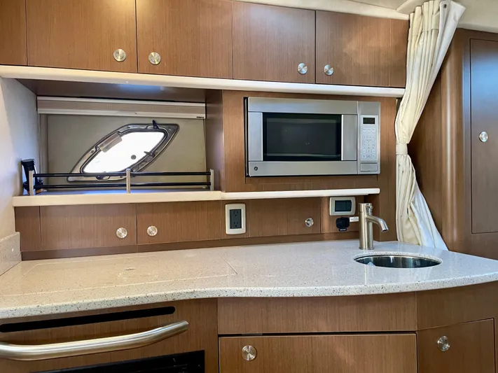 Ilaria Yacht Photos Pics 2014 Sea Ray 330 Sundancer kitchen with microwave, sink, and wooden cabinetry.