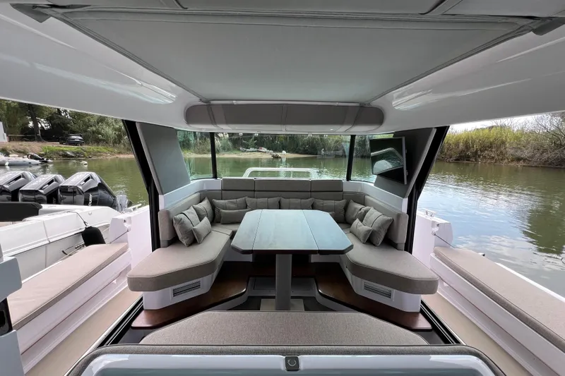  Yacht Photos Pics 2023 Axopar 45 Cross Cabin interior with plush seating and table, overlooking serene water.