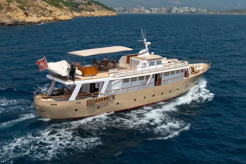 Black Pepper Yacht Photos Pics 1975 Lavagna round stern motoryacht cruising on blue ocean near rocky coastline.