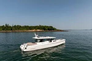 Stock 5 Yacht Photos Pics 2024 Axopar 45 boat cruising on calm waters near a lush, green shoreline.