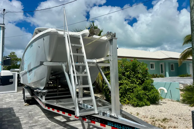 Yacht Photos Pics 2024 World Cat 325 CC boat on trailer, parked near a house with lush greenery.
