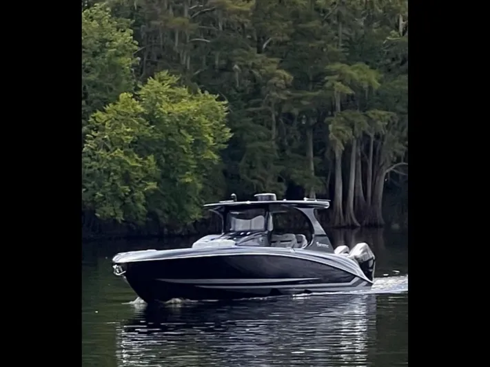  Yacht Photos Pics 2024 Mystic Powerboats M3800 cruising on a serene lake with lush forest backdrop.