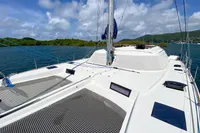 Nautitech 542 catamaran sailing in scenic waters, 2013 model, clear skies, lush green backdrop.