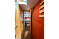 Nautitech 542 yacht interior hallway leading to cozy bedroom, featuring warm wood and orange accents.