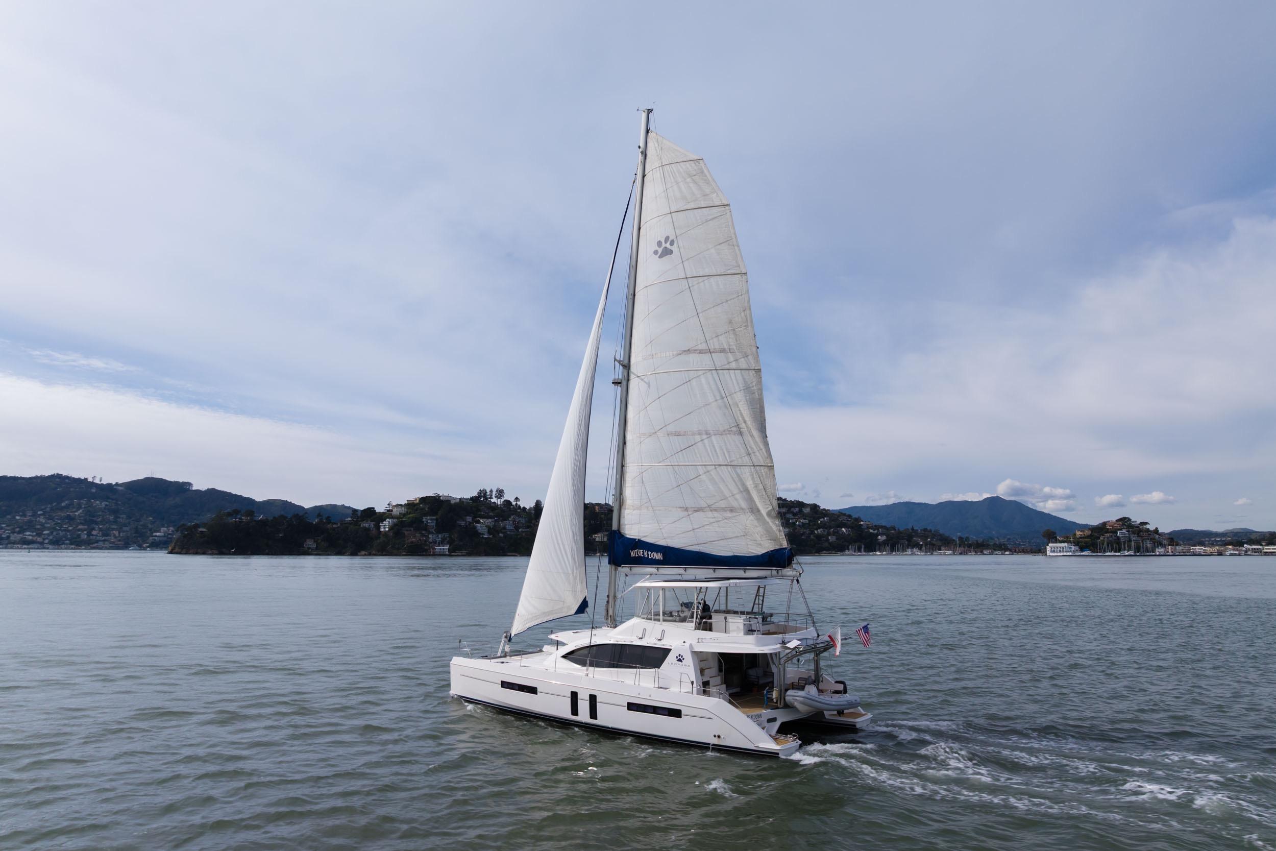 Sailing yacht Leopard 58, 2015 model, cruising on calm waters with scenic hills.
