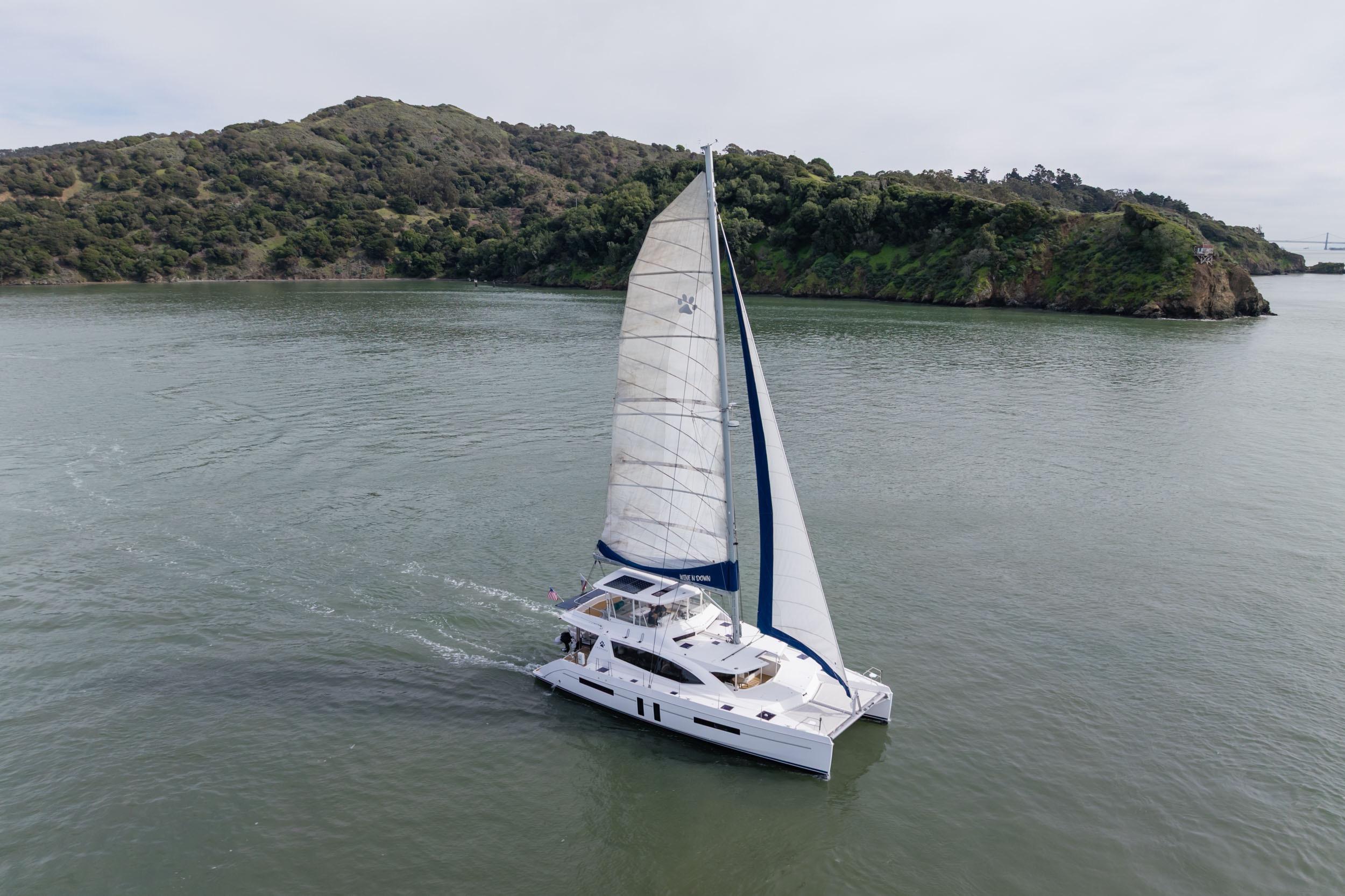 Sailing catamaran Leopard 58, 2015 model, cruising near lush green island.