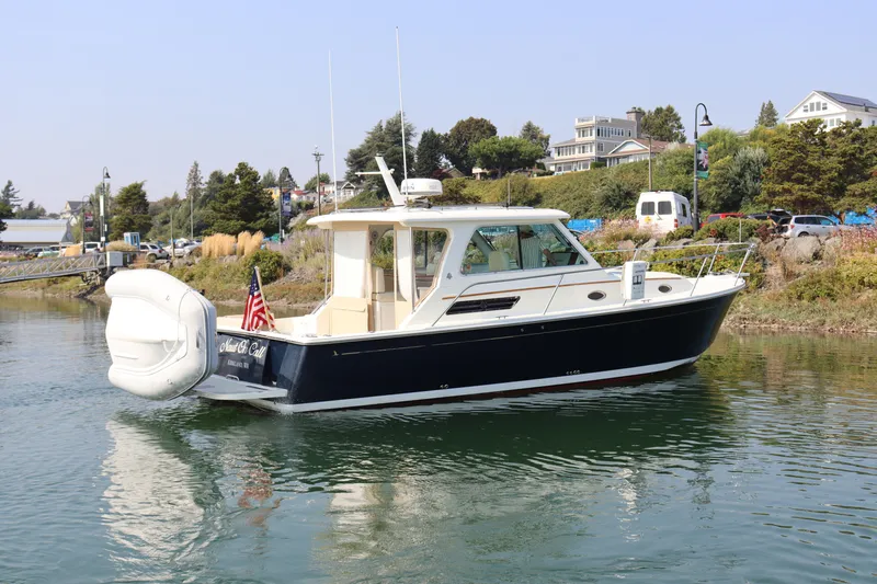 Naut On Call Yacht Photos Pics 2016 Back Cove 34 boat on calm water, with scenic shoreline and houses in the background.